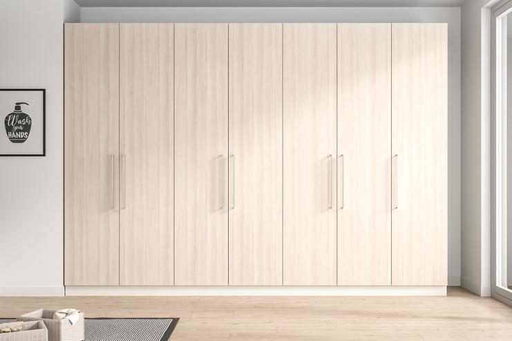 Wandfüllender, maßgeschneiderter Schrank in heller Holzoptik mit minimalistischen Griffen, der nahtlos in das moderne Raumdesign integriert ist.